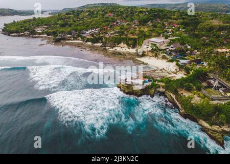 Vue aérienne de la mer surf et des vagues le long de la plage de la station balnéaire de Lembongan avec végétation luxuriante et les bâtiments à la... Banque D'Images