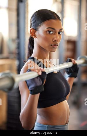 Nous allons dur ici. Photo d'une jeune femme qui s'occupe de poids dans une salle de sport. Banque D'Images