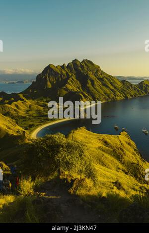 Les voyageurs en haut d'une colline regardant le coucher du soleil avec des bateaux amarrés dans la baie de l'île de Padar dans le parc national de Komodo dans l'archipel de Komodo Banque D'Images