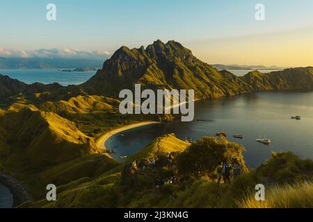 Les voyageurs en haut d'une colline regardant le coucher du soleil avec des bateaux amarrés dans la baie de l'île de Padar dans le parc national de Komodo dans l'archipel de Komodo Banque D'Images