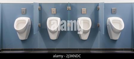 Quatre urinoirs blancs dans une rangée sur un mur bleu dans une salle de repos pour hommes à l'aéroport de Munich ; Munich, Allemagne Banque D'Images