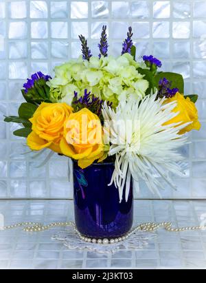 Bouquet de fleurs coupées fraîches dans un vase bleu avec un Doily crocheté et des perles, une variété de fleurs dans l'arrangement, y compris des roses jaunes et W... Banque D'Images