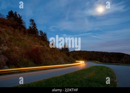 Sous la lune, les phares de voiture s'allument le long de la Blue Ridge Parkway, dans les Blue Ridge Mountains de Caroline du Nord, aux États-Unis Banque D'Images