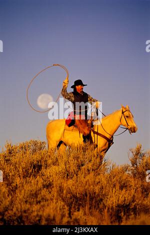Cowboy assis à cheval avec une pleine lune capturée dans son lasso; Seneca, Oregon, États-Unis d'Amérique Banque D'Images