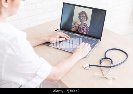 Une femme âgée avec la grippe pour une consultation en ligne avec un médecin. Une femme praticienne passe un appel vidéo avec un patient sur un ordinateur portable. Un retraité Banque D'Images