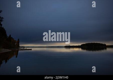 Docks et arbres silhouettés le long d'un rivage et lumière du coucher de soleil reflétée dans l'eau tranquille vue de Meir Road dans le lac de pays, à l'ouest de Princ... Banque D'Images