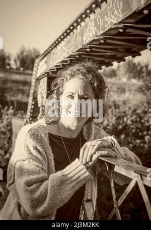 Portrait extérieur d'une femme mûre aux cheveux bouclés debout sur un pont dans un parc; Edmonton, Alberta, Canada Banque D'Images
