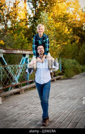 Père donnant à son fils un tour d'épaule dans un parc en automne; Edmonton, Alberta, Canada Banque D'Images