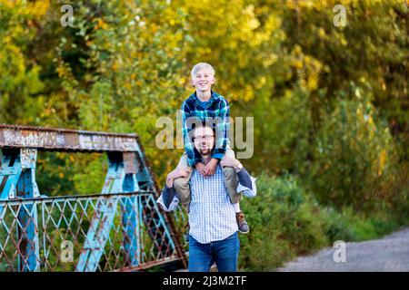 Père donnant à son fils un tour d'épaule dans un parc en automne; Edmonton, Alberta, Canada Banque D'Images