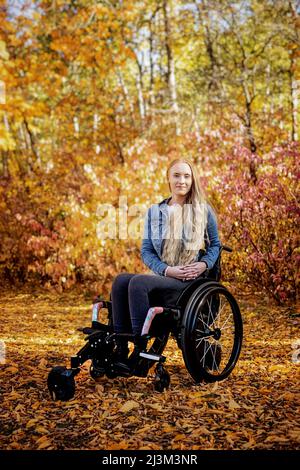 Une jeune femme paraplégique dans son fauteuil roulant dans un parc lors d'une belle journée d'automne; Edmonton, Alberta, Canada Banque D'Images