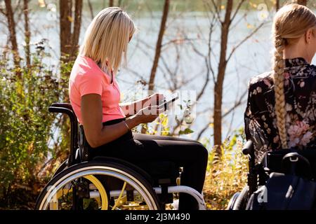 Paraplegic jeune femme utilisant son téléphone intelligent pendant que des amis apprécient une belle journée d'automne à l'extérieur dans un parc de la ville; Edmonton, Alberta, Canada Banque D'Images