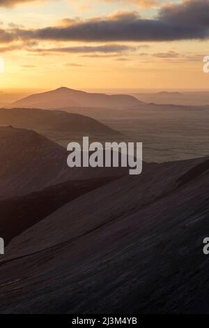 Le soleil se couche sur une série de petites montagnes qui mènent au volcan Fagralsfjall en Islande; Grindavik, Islande Banque D'Images