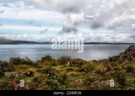 Fougères teintées d'automne et rochers anciens montrent en premier plan à la mer et les montagnes au-delà, ciel nuageux spectaculaire, le son du Jura Banque D'Images