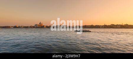 Un coucher de soleil sur l'île de Giudecca tandis qu'un bateau descend le lagon vénitien tranquille, et l'église il Redentore est vue dans la ligne d'horizon Banque D'Images