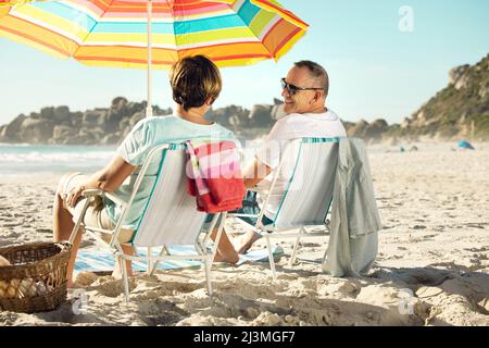 Oubliez vos soucis et rendez-vous à la plage. Photo d'un couple assis sur leurs chaises tout en appréciant une journée à la plage. Banque D'Images