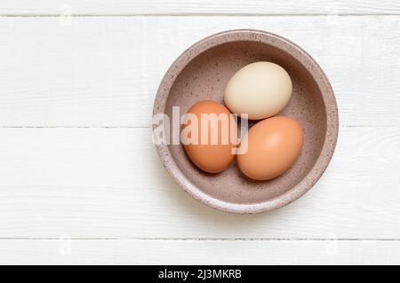 Trois œufs de ferme de poulet dans un bol sur fond de bois blanc. Vue de dessus. Banque D'Images