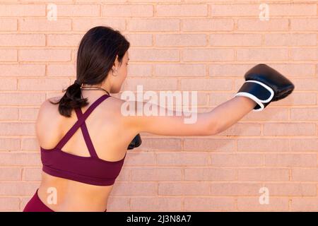 Une jeune femme de race blanche inconnue avec des gants de boxe poinçtue vue du côté et du dos. Le mouvement du bras est capturé sur la photo. La b Banque D'Images