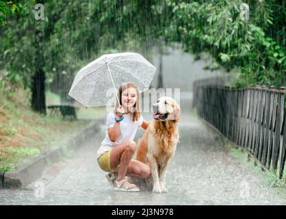 Fille avec un chien de retriever doré sous la pluie assis sous un parapluie à l'extérieur en été. Préteer un enfant avec un chien dans la journée de pluie ensemble Banque D'Images