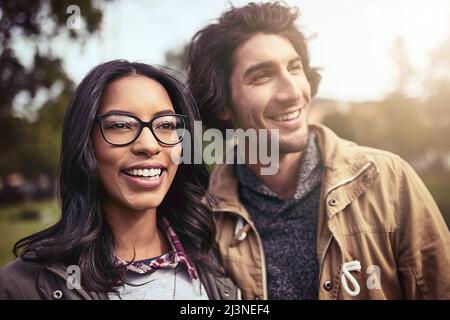 Nous passons du temps tous les jours ensemble. Photo d'un jeune couple gai debout les uns à côté des autres et regardant la vue à l'extérieur dans un parc. Banque D'Images