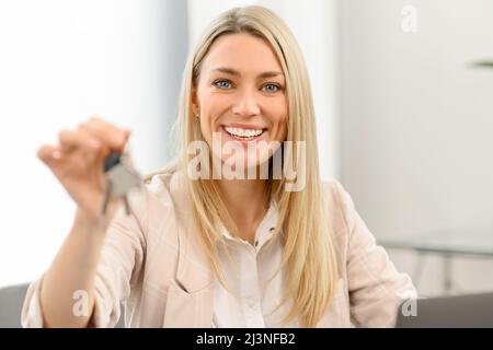 Concept de relocalisation. Une femme excitée se déplaçant dans une nouvelle maison ou un nouvel appartement. Une femme pleine de joie propriétaire regardant la caméra et tenant les clés avec le porte-clés dans sa main Banque D'Images