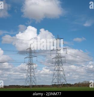 Une paire de tours de transmission contre un ciel bleu avec des nuages blancs moelleux derrière avec une pointe de sol à l'horizon bas Banque D'Images