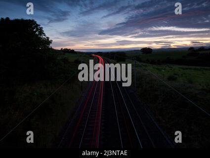 Des feux rouges s'allument au coucher du soleil depuis les feux arrière d'un train sur la ligne principale électrifiée de la côte ouest à Cumbria, au Royaume-Uni Banque D'Images