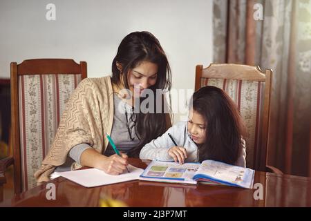 Regardez comment maman le fait. Photo d'une mère qui regarde sa fille faire ses devoirs à la maison. Banque D'Images