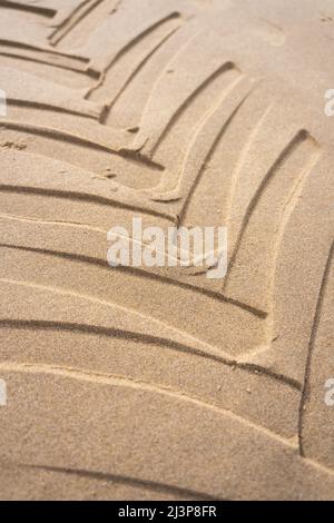 Les empreintes de pneus de tracteur sont incrustées dans une plage de sable avec un motif géométrique. Les chenilles des pneus de véhicules sont en gros plan avec une texture sablonneuse au bord de la mer. Banque D'Images