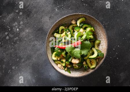 Salade asiatique épicée de concombres brisés avec coriandre fraîche, gingembre, piment, vinaigre noir isolé sur fond noir foncé. Concombres épicés. Popul Banque D'Images