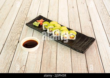 Sushi uramaki Caterpillar rempli d'avocat avec saumon norvégien, algues nori, fromage frais et sauce soja sur table blanche Banque D'Images