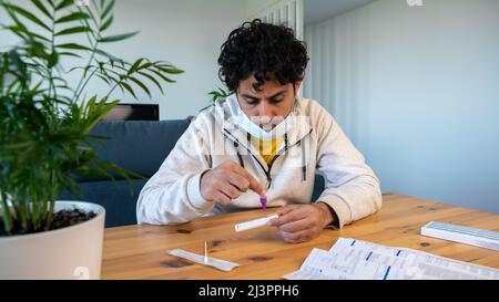 Un homme portant un masque plaçant l'échantillon dans le dispositif de test diagnostique de l'antigène covid-19 à la maison. Kit de cassette pour auto-test pour vérifier l'entrée Banque D'Images