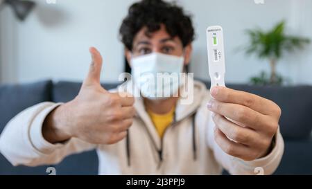 L'homme caucasien qui fait un geste de pouce vers le haut fait un dispositif rapide de test à la maison pour Covid19 virus avec un résultat négatif. Cassette d'antigène de pcr express Banque D'Images