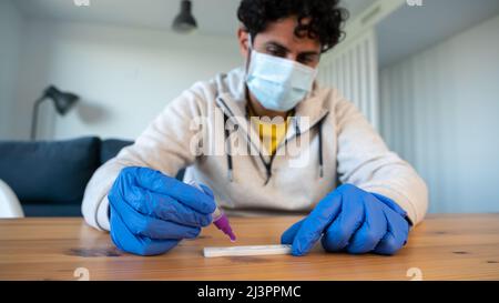 Un homme portant un masque et des gants en latex plaçant l'échantillon dans le dispositif de test diagnostique de l'antigène covid-19. Kit avec kit de cassette pour auto-test pour vérifier t Banque D'Images