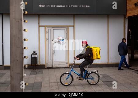 Moscou, Russie. 9th avril 2022. Un messager du service de livraison Yandex EDA se trouve à vélo le long de la rue Novy Arbat, sur fond d'une librairie fermée Respublika (Eng: Republic) à Moscou, en Russie. L'inscription au-dessus de l'entrée fermée indique « Book Music perspective » Banque D'Images