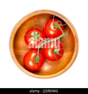 Tomates cerises rouges, dans un bol en bois. Tomates mûres, petites, rondes, cocktail sur la vigne, de la taille d'un bout de pouce, avec un goût super sucré. Banque D'Images