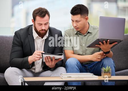 Formuler des plans novateurs. Photo de deux hommes d'affaires qui passent par la paperasse tout en utilisant un ordinateur portable ensemble dans un bureau. Banque D'Images