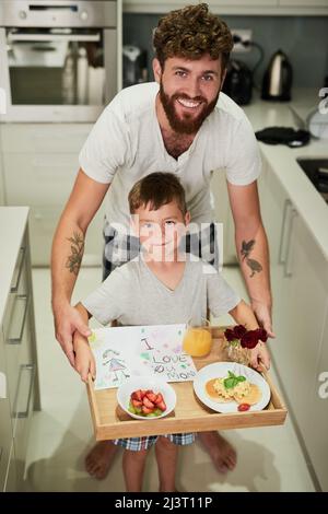 Les mamans vont être si surpris. Photo d'un adorable petit garçon tenant un plateau de petit déjeuner avec son père pour la fête des mères. Banque D'Images