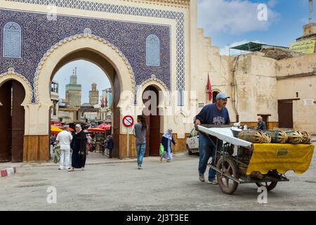 Fes, Maroc. Vendeur de fruits poussant son panier de fruits par la porte Bab Boujeloud, entrée à Fès El-Bali, la vieille ville. Le minaret de la Bou Inan Banque D'Images