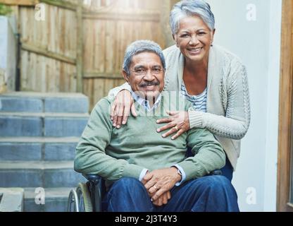 Shes signifie le monde pour moi. Portrait d'un homme âgé gai assis dans un fauteuil roulant tout en étant tenu par sa femme aimante dehors à la maison pendant le Banque D'Images