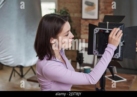 Jeune femme opérateur qui choisit des configurations à LED tout en se préparant pour la prise de vue en studio Banque D'Images