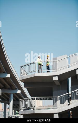 Grand projet de construction en ville : des ingénieurs très occupés travaillant avec Blueprint et se tenant sur le site de construction de gratte-ciel sans murs Banque D'Images