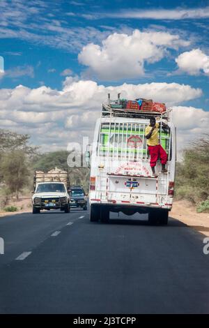 Sénégal, sécurité routière. Homme mangeant un Mango tout en se reposant sur une rampe à l'arrière d'un bus. Pas de ceinture de sécurité ici! Banque D'Images