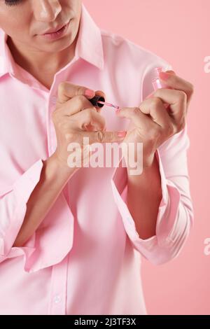 Image rognée d'un jeune homme sérieux appliquant du vernis à ongles rose Banque D'Images