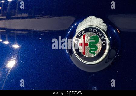 L'écusson Alfa Romeo à l'arrière d'un véhicule bleu, vu la nuit chez un concessionnaire automobile. Banque D'Images