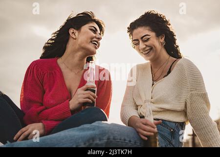 Joyeux jeunes amies sans souci à l'extérieur boire des bières - deux jeunes femmes seules joyeusement passer du temps à l'extérieur à la périphérie de la ville, près de la Banque D'Images