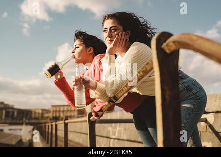 Les meilleurs amis boivent des bières à l'extérieur - deux jeunes femmes penchées sur un balustrade boivent des bières et passent sans soucis leur temps à discuter dans la détente Banque D'Images