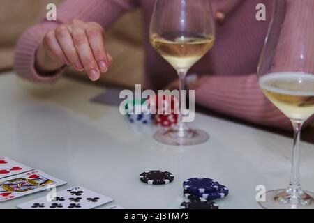 Femme fait un mouvement dans un jeu de poker. Jetons, cartes, verres de champagne sur la table avec réflexion. Photographie de style de vie Banque D'Images