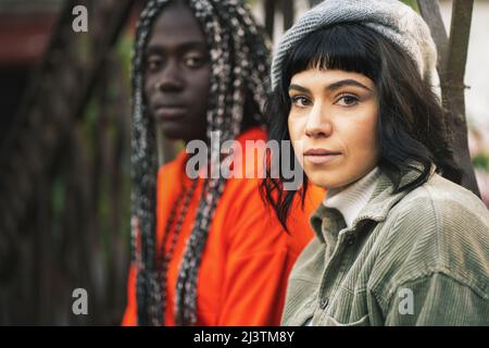 Portrait de deux filles de 20 ans de différentes courses tout en étant assis à l'extérieur, regardant la caméra -. Amitié et intégration concept Banque D'Images