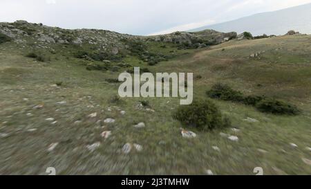 Vue de dessus des collines verdoyantes avec des rochers. Action. Un drone survole de belles collines verdoyantes par temps nuageux. Drone volant sur de belles collines en été Banque D'Images