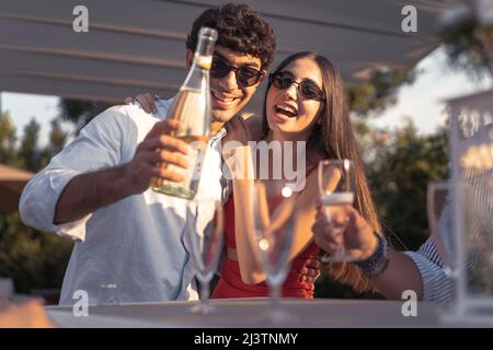Couple de jeunes engagés qui versent du champagne dans des flûtes célébrant leur amour - amis gaies buvant du vin mousseux souriant et du havi Banque D'Images